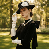 Load image into Gallery viewer, icevellyyy black velvet evening dress with long sleeves, bow detail, and white opera gloves. Model wears pearls and a wide-brimmed hat.