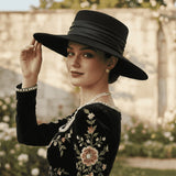 Load image into Gallery viewer, Black felt wide-brimmed hat with satin ribbon band, worn by a model in an embroidered velvet dress.